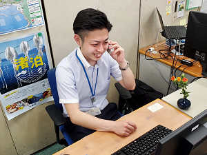 業務中の様子(パソコンを確認しながら、関係団体と電話している。傍らには紅花の一輪挿し)